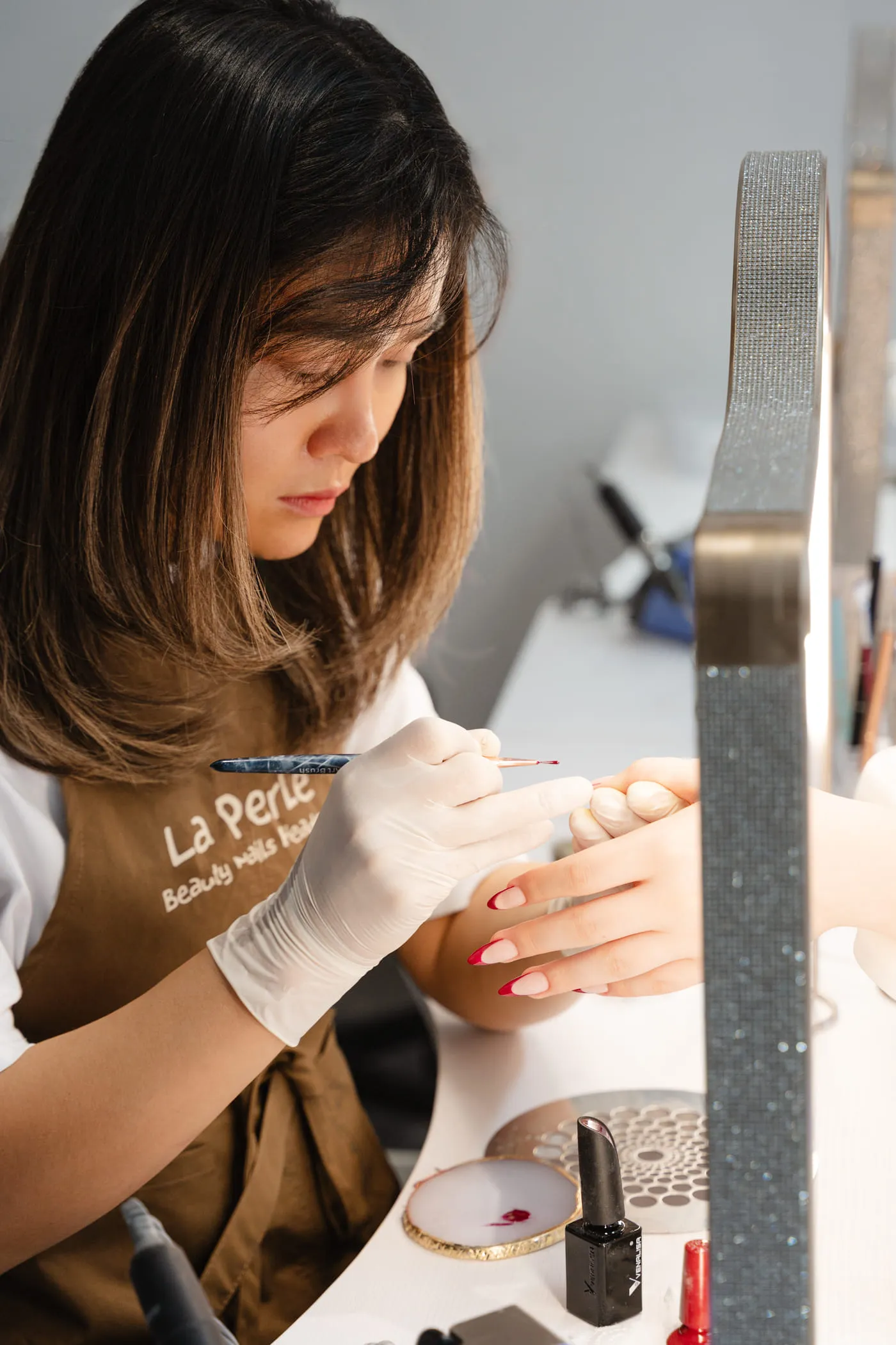 Nageldesignerin von La Perle bemalt in Handschuhen einen Nagel